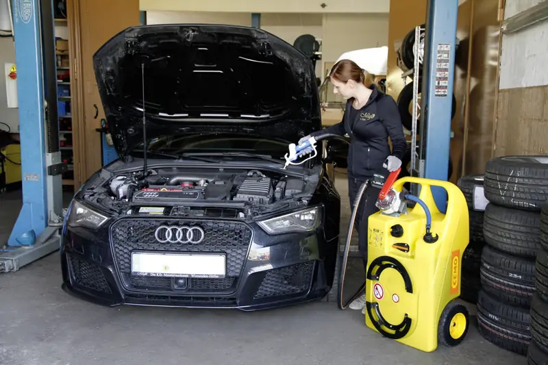 Service am geöffneten Motorraum eines Audi in der Werkstatt Miglo, daneben Reifenregal